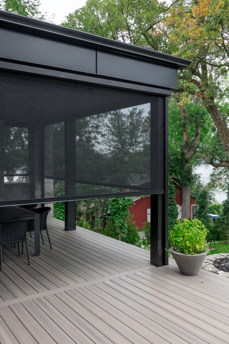 Outdoor roller shade over a modern deck surrounded by trees in daylight